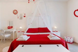 A bedroom with a bed, bedside tables, a desk, a chair, a mirror, and a clock on the wall.