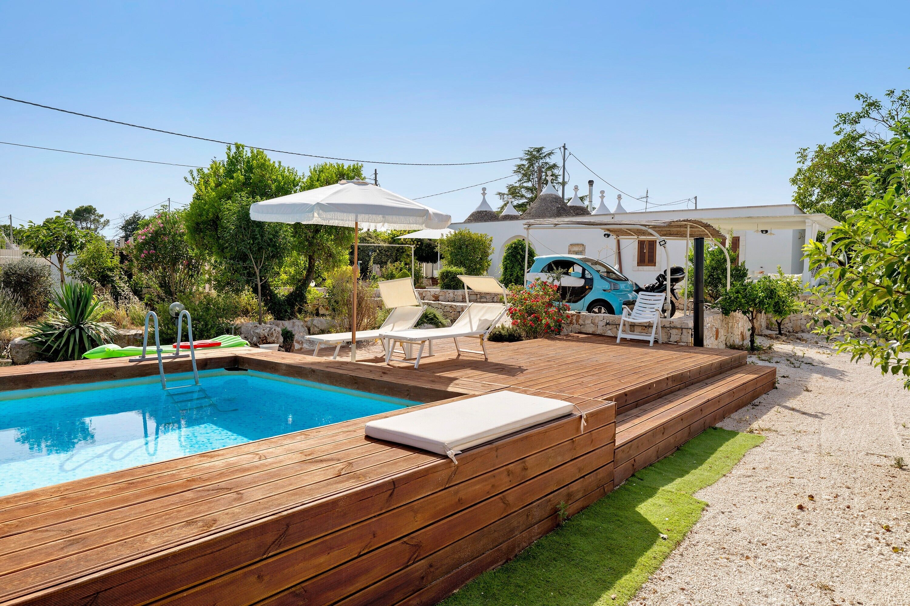 Une piscine avec une terrasse en bois, des chaises longues et un patio couvert.