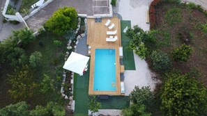 Luftaufnahme eines Poolbereichs mit Holzterrasse, Liegestühlen und einer überdachten Sitzgruppe.