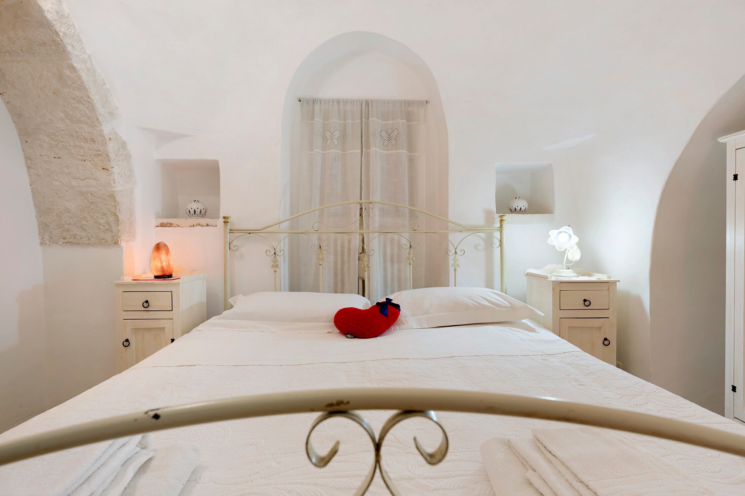 Een slaapkamer met een bed, twee nachtkastjes, een wandplank en een raam met gordijnen.