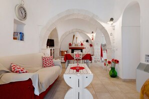 A living room with a sofa, a dining table, and a kitchen area visible through an archway. - Trullo 'Vito with Pool' with Private Pool, Shared Terrace and Wi-Fi (Martina Franca)