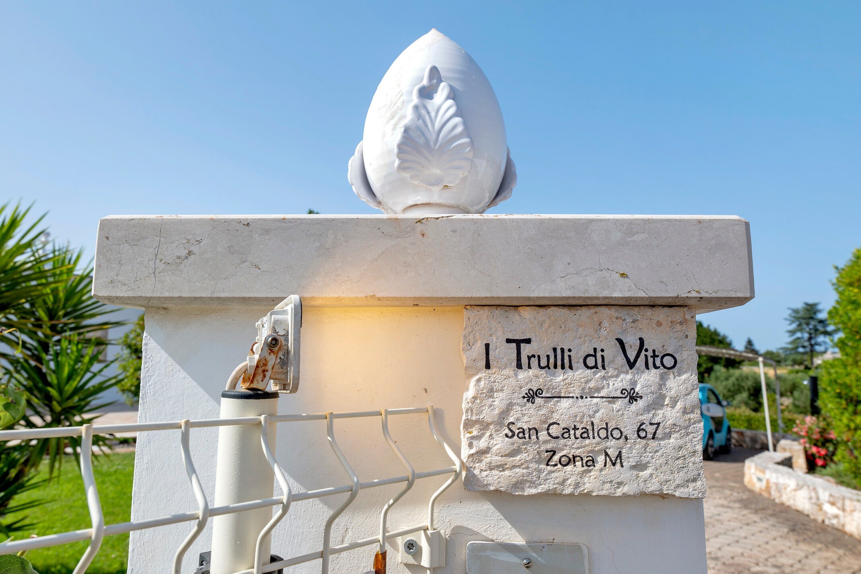 Een wit stenen monument met een bladachtige bovenkant en een plaquette met de tekst 'I Trulli di Vito, San Cataldo, 67, Zona M'.