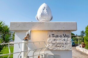 A white stone monument with a leaf-shaped top and a plaque reading 'I Trulli di Vito, San Cataldo, 67, Zona M'.
