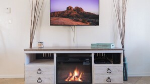 A modern living room with a flat-screen TV mounted on the wall, a fireplace below, and a small table with decorative branches. - Adventure Loft: Near Trails, Pool and Golf (Sedona)