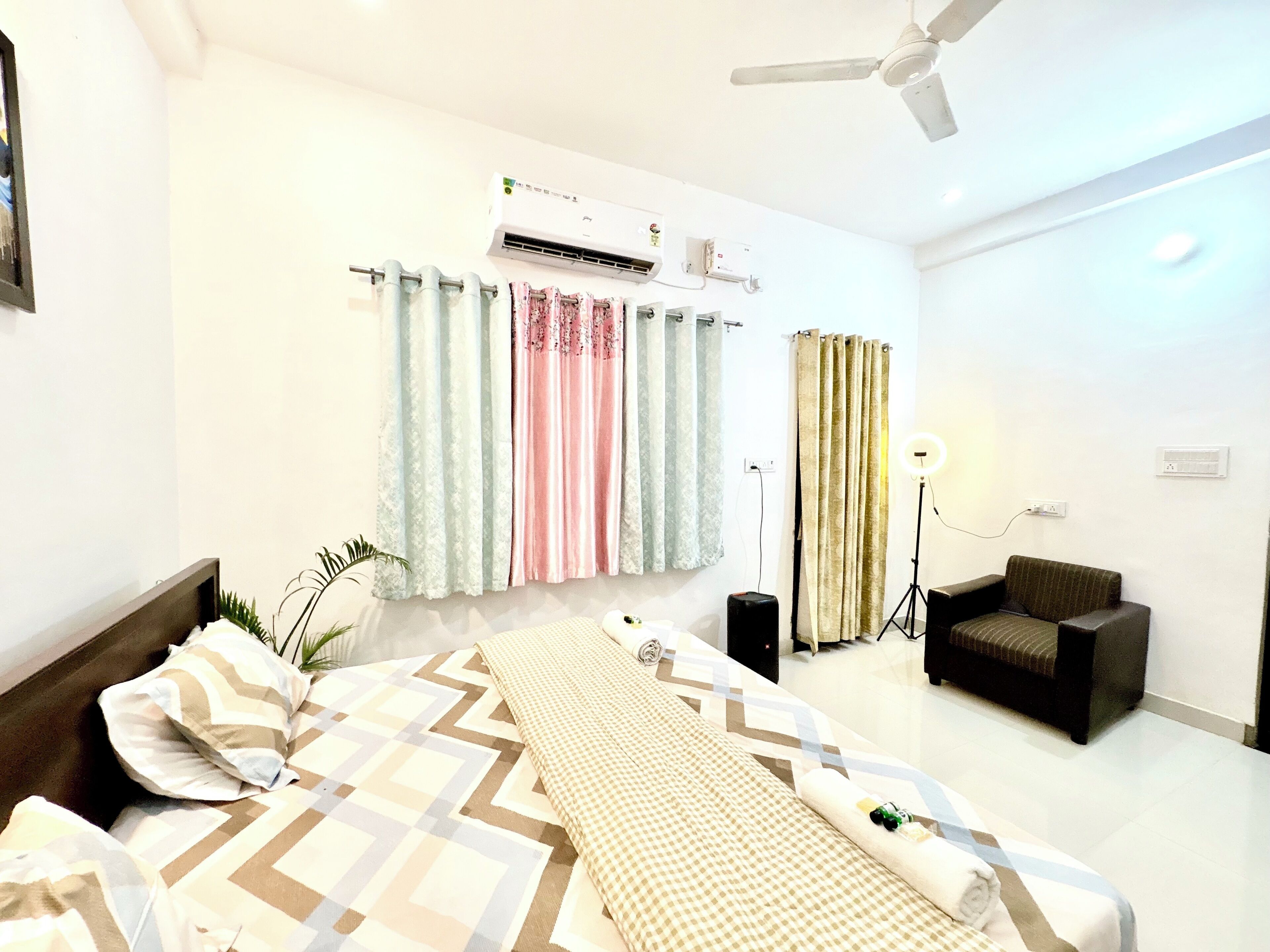 A hotel room with a bed, a chair, an air conditioning unit, curtains, and a ceiling fan.
