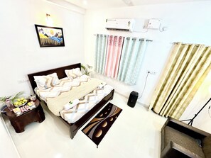 A neatly arranged bedroom with a bed, bedside table, air conditioning units, curtains, and a speaker. - Majestic Guest House (Varanasi)