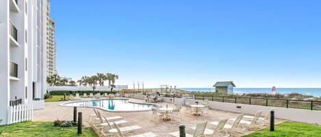 A pool area with lounge chairs and a view of the beach.