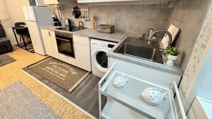 Una cocina compacta con armarios blancos, horno integrado, lavadora y un lavamanos.