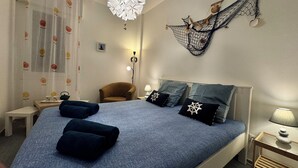 Un dormitorio con cama, almohadas, una silla, escritorio, lámpara y decoración en la pared.