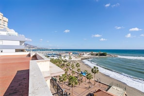 A coastal hotel with a terrace overlooking the beach, palm trees, and a view of the sea and distant cityscape. - Marvelous Waterfront apt in Fuengirola - Ref 73 (Fuengirola)