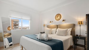 Ein Hotelzimmer mit einem großen Bett, zwei Nachttischen, einem Schreibtisch und einem Fenster mit Blick auf die Stadt.