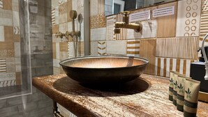 Un bagno con un lavabo grande, rotondo e scuro su un piano d'appoggio strutturato, un box doccia in vetro e piastrelle decorate sulle pareti.