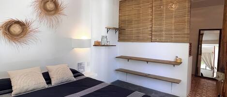 Un dormitorio moderno con una cama grande, mesitas de noche, una lámpara colgante y un estante en la pared.