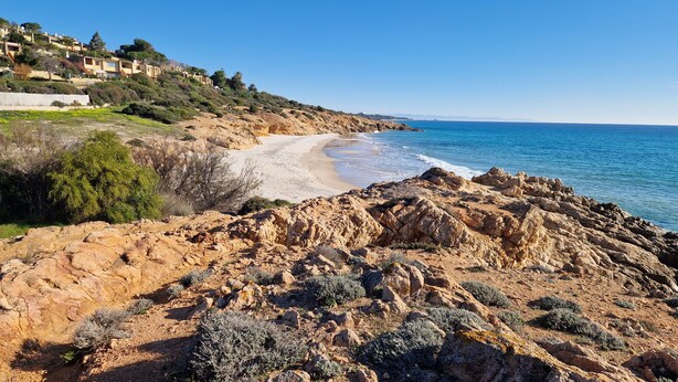 Paesaggio costiero con terreno roccioso, spiaggia sabbiosa e un pendio con edifici.