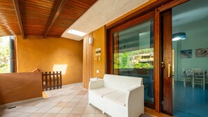 Una stanza con un divano bianco, soffitto in legno, una porta in vetro e pavimento piastrellato.