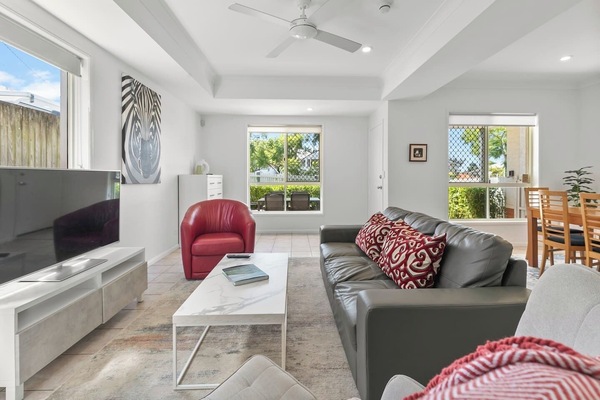 Sink into comfort in this sunlit living room with vibrant red accents, comfortable seating and a TV—a perfect space to relax or enjoy a movie night.