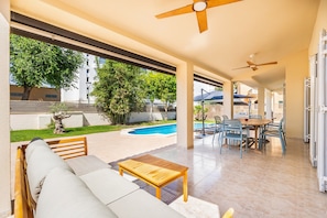 Un espacio al aire libre techado con piscina, mesa de comedor y sofá.