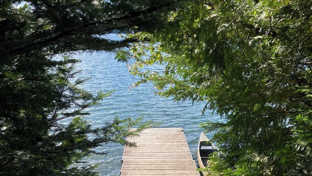 A wooden dock leading to a body of water, with a chair and a kayak on the dock.