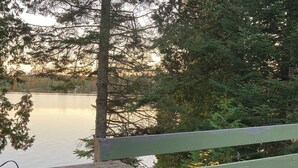 A wooden deck with a bench overlooking a calm lake, surrounded by dense trees.