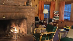 A cozy living room with a brick fireplace, wicker furniture, and a bookshelf.