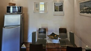 Un comedor con techo de piedra, refrigerador, microondas, mesa de vidrio y cuatro sillas.