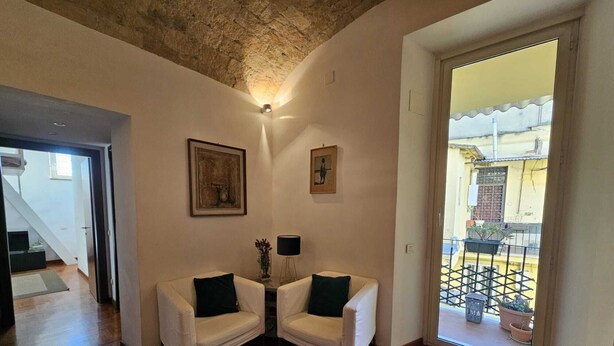 Un salón con dos sillones blancos, un tapete estampado y un techo con detalles de piedra a la vista.