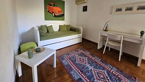 Un espacio habitable compacto con un sofá blanco, una mesita, un escritorio y una alfombra estampada.