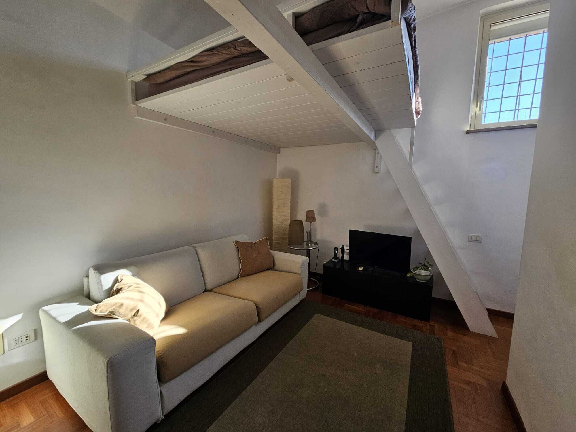 Uma sala de estar com sofá, televisão, luminária e janela.