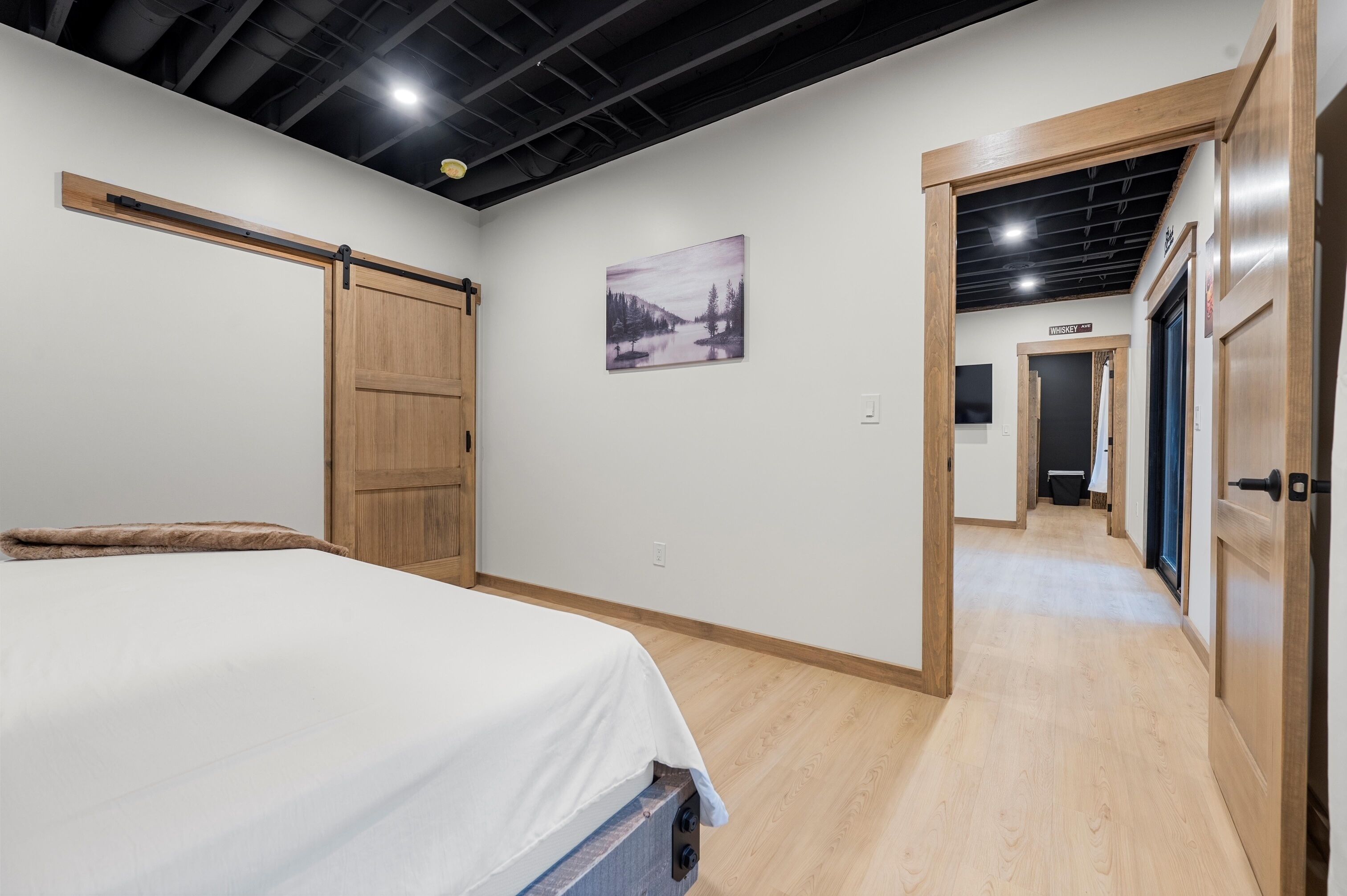 A bedroom with a bed, a sliding door, a hallway, and a sign indicating a whiskey room.