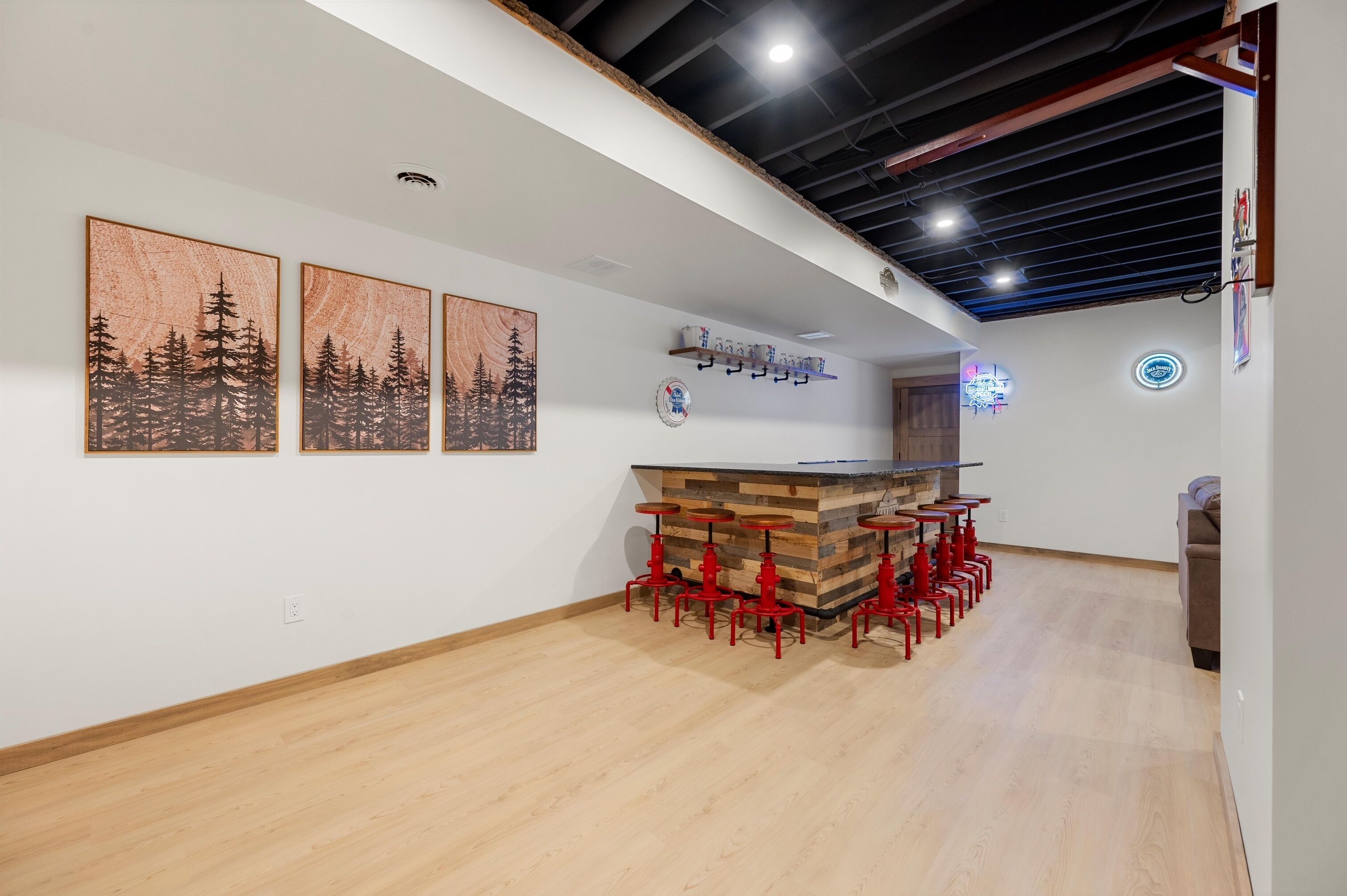 A modern kitchen with a wooden island, red bar stools, and three framed forest paintings on the wall.