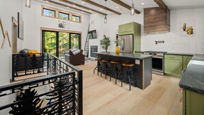 A modern kitchen with a central island, green cabinets, stainless steel appliances, and a wooden ceiling. - Riverside Lodge, a Modern Adirondack Getaway (Boonville)
