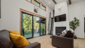 A modern living room with a brown leather sofa, a yellow throw pillow, and a fireplace. - Riverside Lodge, a Modern Adirondack Getaway (Boonville)