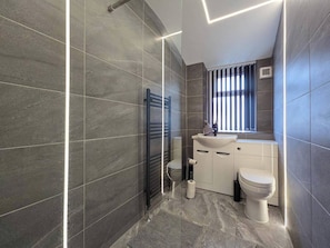 Une salle de bain moderne avec des murs recouverts de carreaux foncés, un porte-serviettes noir, un lavabo blanc et des toilettes.