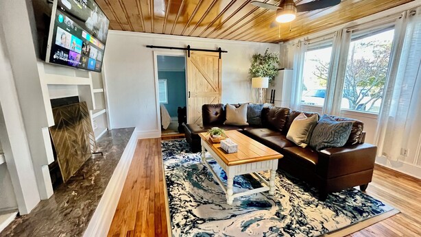 Un salon avec un plafond en bois, un canapé en cuir marron, une table basse et une grande fenêtre.