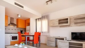 A modern kitchen with orange cabinets, a dining table with red chairs, a TV on a wooden stand, and a large window with curtains. - Apartment 'Tropikana I' with Shared Pool, Wi-Fi and Air Conditioning (Miami Platja)