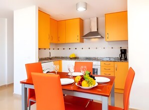 A modern kitchen with orange cabinets, a dining table with orange chairs, and a fruit bowl on the table.