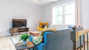 A living room with a television, a yellow chair, a blue sofa, a wooden coffee table, and a ceiling fan. - Charming 4-bedroom house with AC and WiFi in Winston-Salem (Winston-Salem)