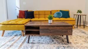 A living room with a mustard yellow sectional sofa, a wooden coffee table, and a patterned rug. - Charming 4-bedroom house with AC and WiFi in Winston-Salem (Winston-Salem)
