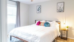 A bedroom with a bed, a ceiling fan, a bedside table with a lamp, and two framed pictures on the wall. - Charming 4-bedroom house with AC and WiFi in Winston-Salem (Winston-Salem)