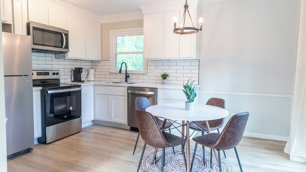 A modern kitchen with white cabinets, stainless steel appliances, a round dining table with chairs, and a chandelier. - Charming 4-bedroom house with AC and WiFi in Winston-Salem (Winston-Salem)