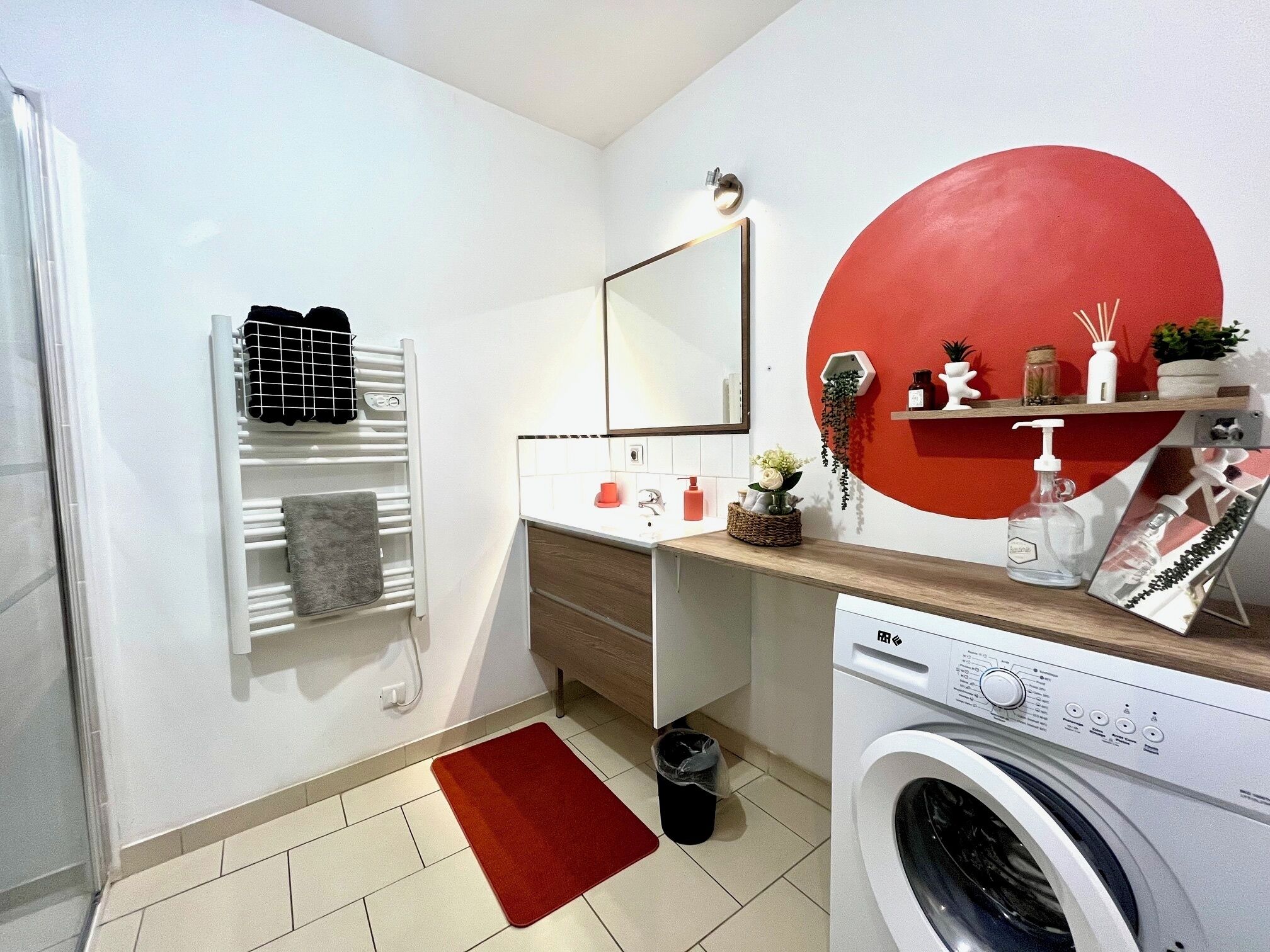 Uma casa de banho compacta e moderna, com máquina de lavar roupa, porta-toalhas, espelho e uma parede de destaque vermelha.