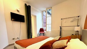 Moderni hotellihuone, jossa on sänky, seinälle asennettu televisio, ikkuna, josta on näkymä, sekä yöpöytä lampulla.