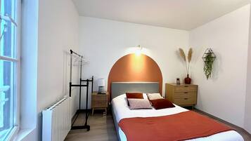 Een slaapkamer met een bed, een radiator, een nachtkastje, een lamp en een plant aan de muur.