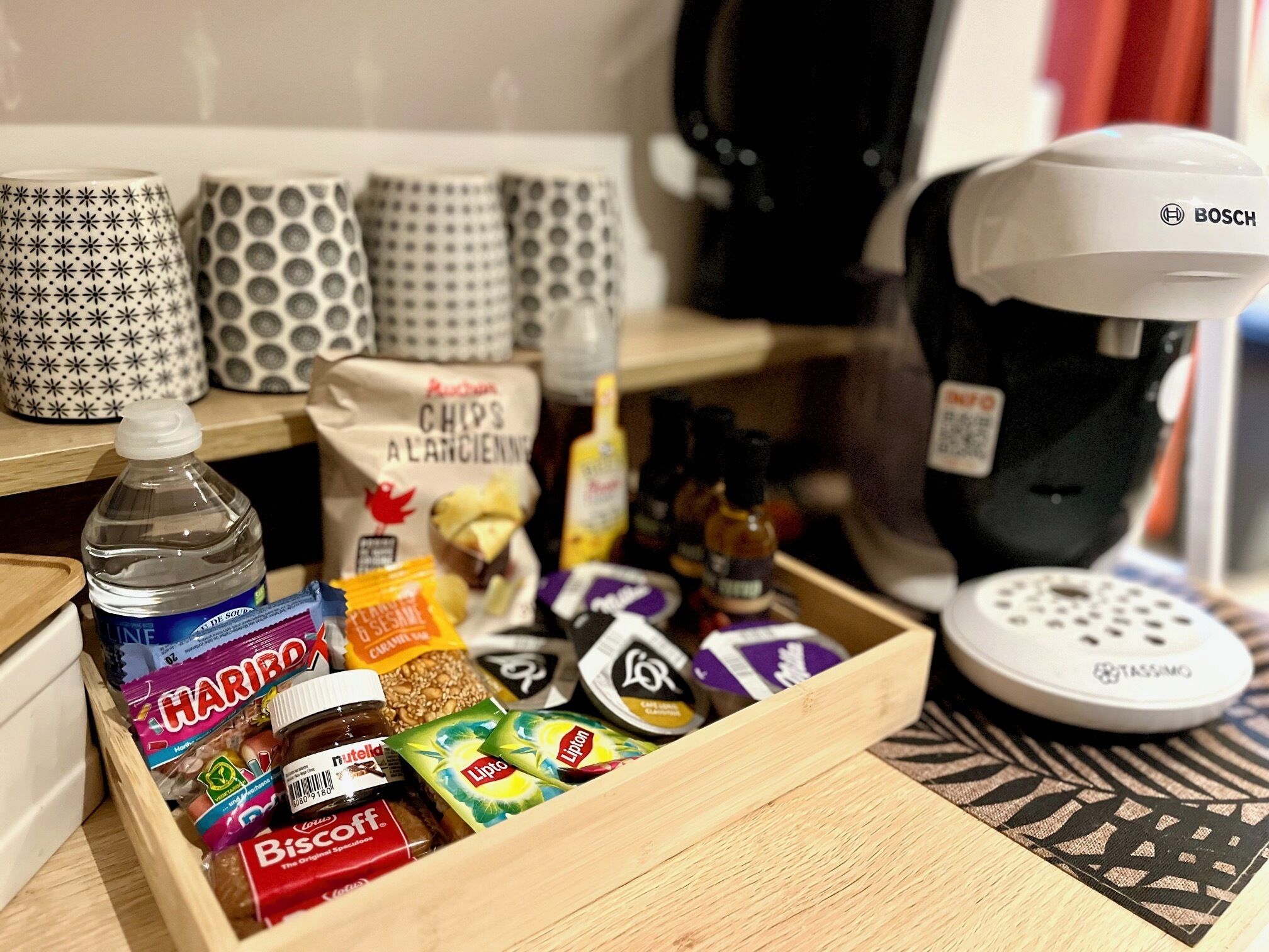 Eine Küchenarbeitsplatte mit Kaffeemaschine, einer Schublade voller Snacks und gemusterten Tassen.