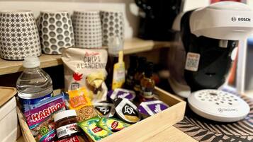 Eine Küchenarbeitsplatte mit Kaffeemaschine, einer Schublade voller Snacks und gemusterten Tassen.