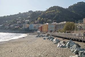 Una spiaggia con un litorale roccioso, una passerella di legno e edifici colorati sullo sfondo.