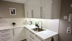 Una cocina compacta con gabinetes blancos, un lavamanos de acero inoxidable y una pequeña encimera.