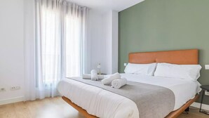 Ein modernes Hotelzimmer mit einem großen Bett, einer grünen Akzentwand und einem Fenster mit transparenten Vorhängen.