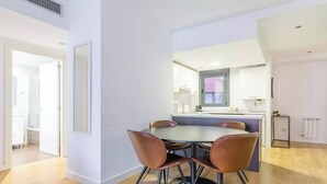 Eine moderne Küche mit einer zentralen Kochinsel, einem Essbereich mit rundem Tisch und vier Stühlen sowie einem sichtbaren Fenster.