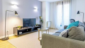 Ein modernes Wohnzimmer mit Flachbildfernseher, einer Couch, einem Couchtisch und einer Stehlampe.